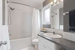 This bright and clean bathroom features a white tiled shower/tub combo with a curved shower rod and a white shower curtain.