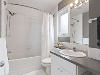 This bright and clean bathroom features a white tiled shower/tub combo with a curved shower rod and a white shower curtain.