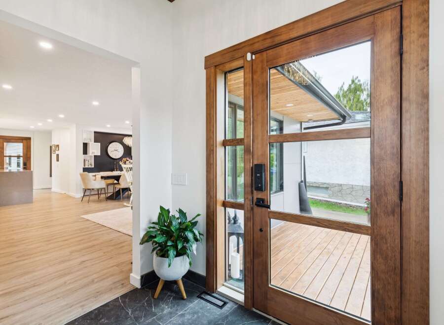 Step into a beautifully designed entryway featuring a stunning wooden double door with glass panels, offering a glimpse of the outdoor deck.