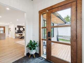Step into a beautifully designed entryway featuring a stunning wooden double door with glass panels, offering a glimpse of the outdoor deck.