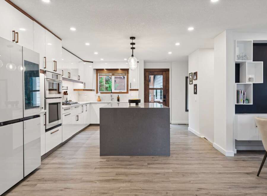 Experience modern living in this stunning kitchen featuring sleek white cabinetry, a large grey island, and integrated appliances.