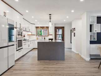 Experience modern living in this stunning kitchen featuring sleek white cabinetry, a large grey island, and integrated appliances.