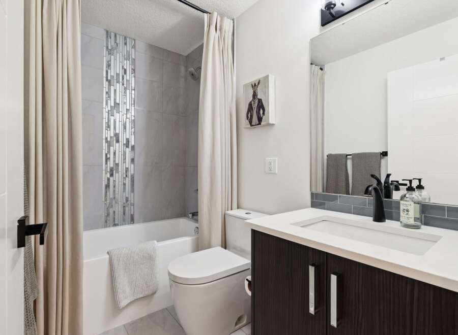 This modern bathroom features a sleek vanity with a white countertop and dark wood cabinetry, complemented by a stylish black faucet.