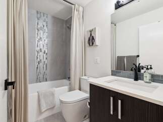 This modern bathroom features a sleek vanity with a white countertop and dark wood cabinetry, complemented by a stylish black faucet.