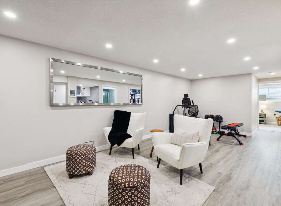 This spacious basement features a comfortable seating area with two white armchairs and patterned ottomans, perfect for relaxation.