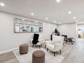 This spacious basement features a comfortable seating area with two white armchairs and patterned ottomans, perfect for relaxation.