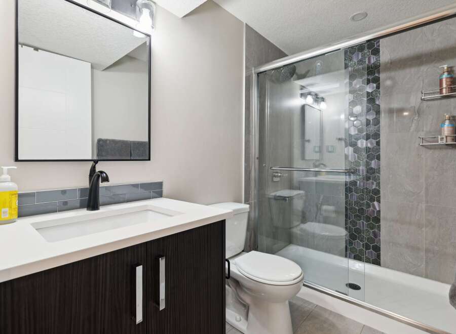 This modern bathroom features a sleek vanity with a dark wood cabinet and a white countertop, complemented by a black faucet and a large mirror.