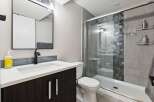 This modern bathroom features a sleek vanity with a dark wood cabinet and a white countertop, complemented by a black faucet and a large mirror.