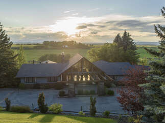 Experience luxury living in this stunning estate, featuring a grand entrance with a soaring glass facade and exposed wooden beams.