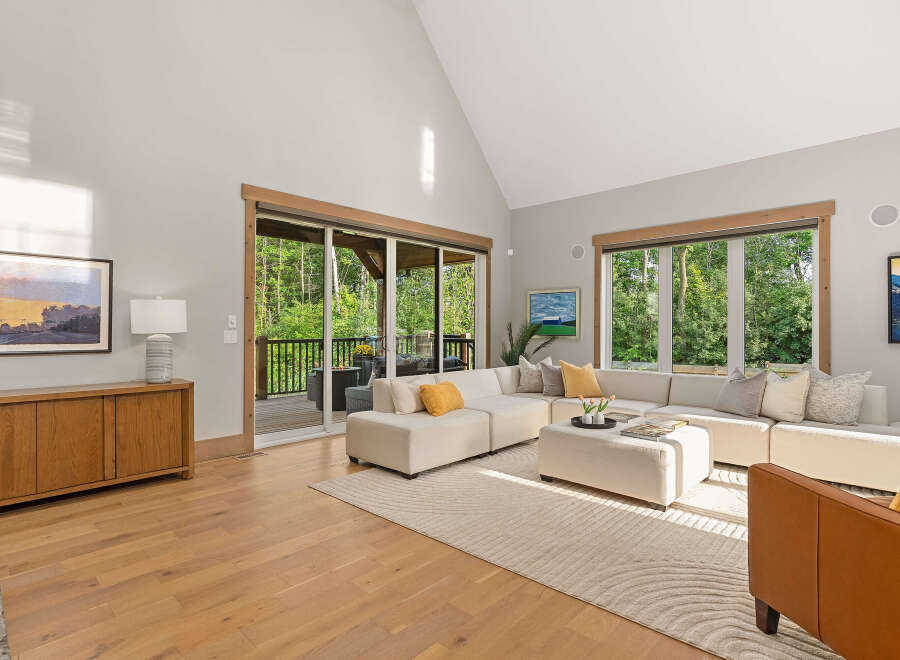 Experience seamless indoor-outdoor living in this stunning living room, featuring a spacious sectional sofa and large sliding glass doors that open to a lush, wooded backyard.