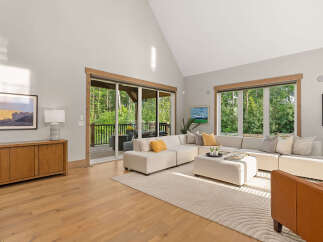 Experience seamless indoor-outdoor living in this stunning living room, featuring a spacious sectional sofa and large sliding glass doors that open to a lush, wooded backyard.