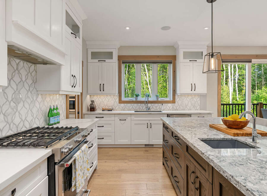 Experience luxury in this stunning modern kitchen, featuring sleek white cabinetry, a decorative tile backsplash, and a large granite island perfect for entertaining.