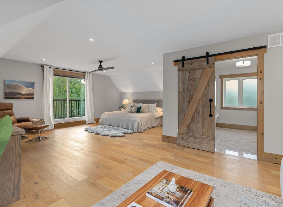 Experience modern rustic charm in this spacious bedroom featuring a vaulted ceiling and a stylish barn door leading to an en-suite bathroom.