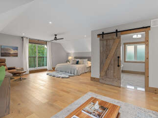 Experience modern rustic charm in this spacious bedroom featuring a vaulted ceiling and a stylish barn door leading to an en-suite bathroom.