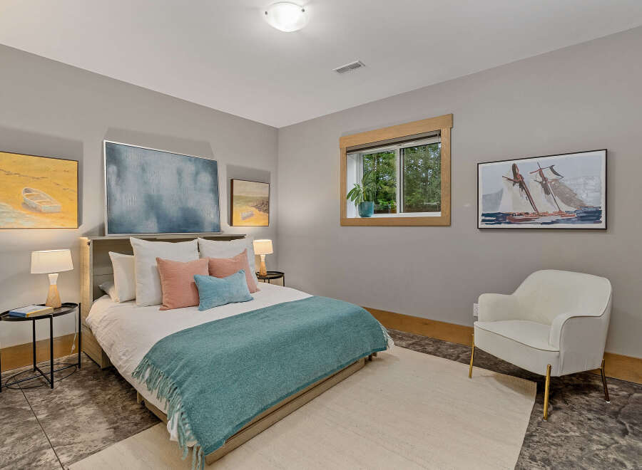 This serene bedroom offers a tranquil retreat with its calming gray walls and comfortable queen-size bed adorned with plush pillows and a cozy teal throw.