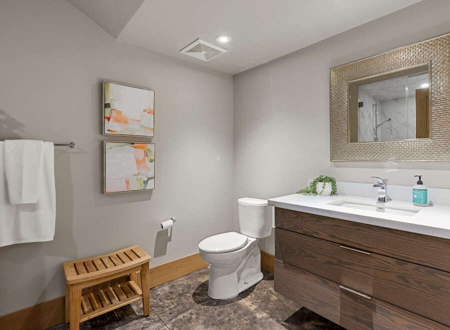This modern bathroom features a sleek vanity with dark wood cabinetry and a white quartz countertop, complemented by a minimalist sink and chrome faucet.