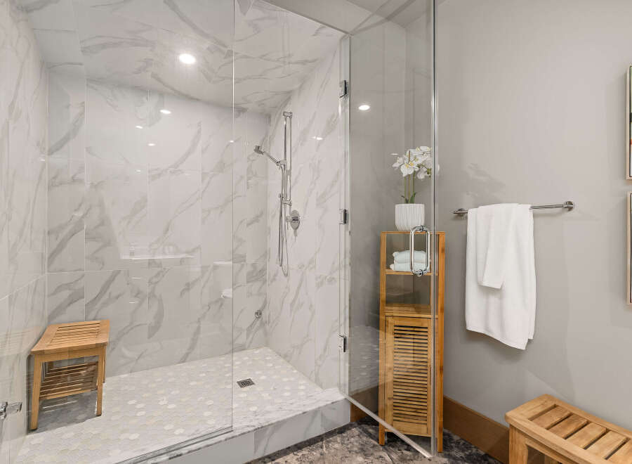 Experience luxury in this modern bathroom featuring a spacious walk-in shower with elegant marble-look tiles and a convenient wooden bench.