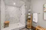 Experience luxury in this modern bathroom featuring a spacious walk-in shower with elegant marble-look tiles and a convenient wooden bench.