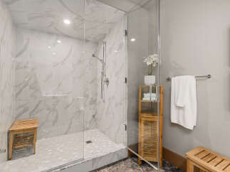 Experience luxury in this modern bathroom featuring a spacious walk-in shower with elegant marble-look tiles and a convenient wooden bench.