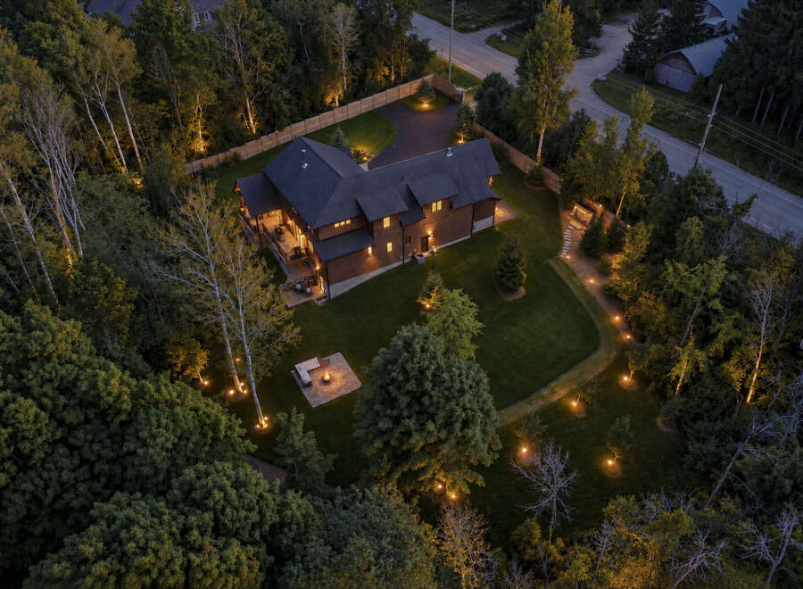 Experience luxury living in this stunning wooded estate, featuring a spacious modern home with expansive decks and a beautifully lit outdoor seating area with a fire pit.