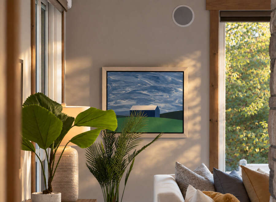 This living room features a modern aesthetic with a large abstract painting of a blue barn and sky above a white sofa.