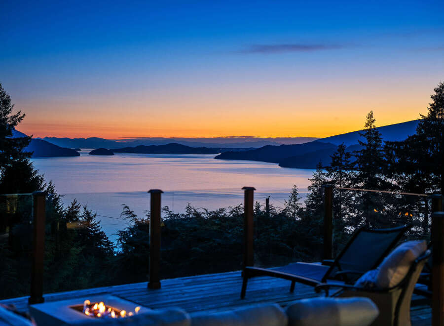 Experience breathtaking sunset views from this stunning property, featuring a spacious deck with a fire pit and comfortable lounge chairs.