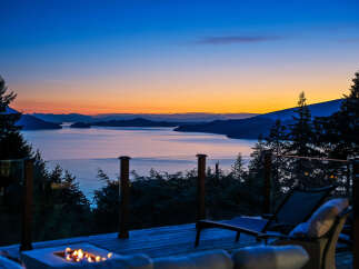 Experience breathtaking sunset views from this stunning property, featuring a spacious deck with a fire pit and comfortable lounge chairs.