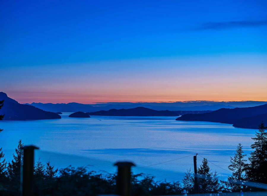 Experience breathtaking twilight views from this stunning property, featuring a serene waterfront and majestic mountain backdrops.