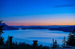 Experience breathtaking twilight views from this stunning property, featuring a serene waterfront and majestic mountain backdrops.