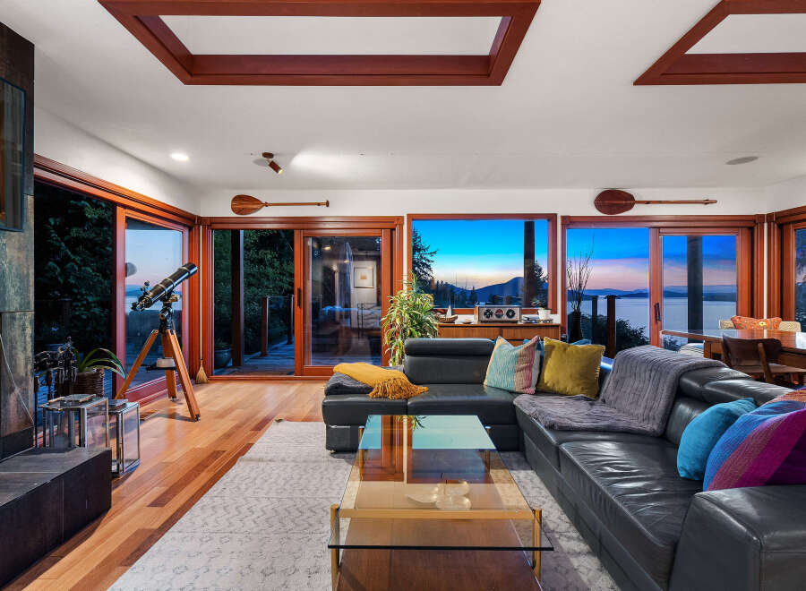 Experience breathtaking sunset views from this stunning living room, featuring a sleek black leather sectional and a glass coffee table.