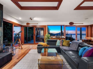 Experience breathtaking sunset views from this stunning living room, featuring a sleek black leather sectional and a glass coffee table.