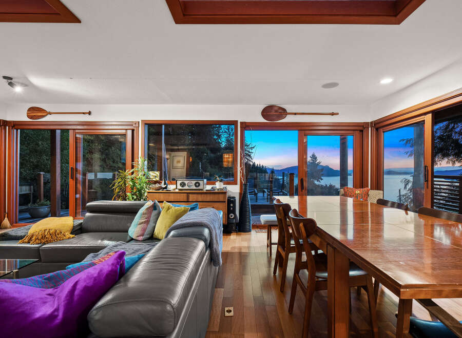 Experience breathtaking sunset views from this stunning living and dining area, featuring a spacious leather sectional and a large wooden dining table perfect for gatherings.