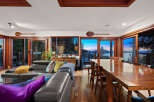 Experience breathtaking sunset views from this stunning living and dining area, featuring a spacious leather sectional and a large wooden dining table perfect for gatherings.