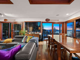 Experience breathtaking sunset views from this stunning living and dining area, featuring a spacious leather sectional and a large wooden dining table perfect for gatherings.