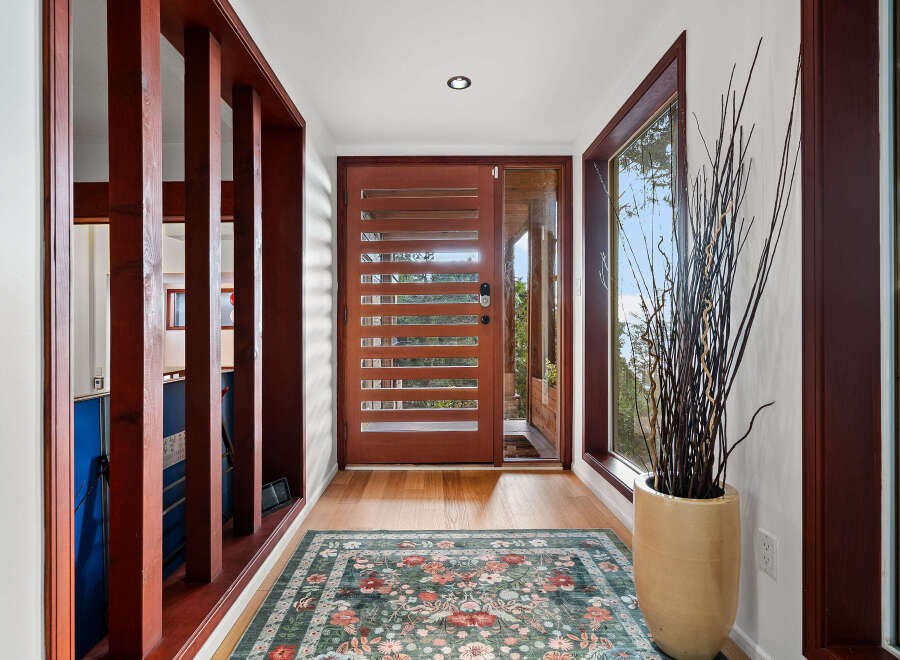 Step into this inviting entryway featuring a modern wooden door with horizontal slats, complemented by a large window offering scenic views.