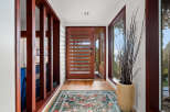 Step into this inviting entryway featuring a modern wooden door with horizontal slats, complemented by a large window offering scenic views.