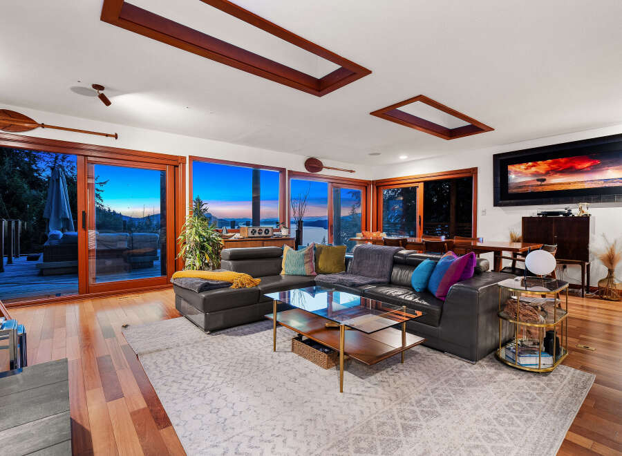 Experience breathtaking sunset views from this stunning living room, featuring expansive windows that open to a serene waterfront landscape.