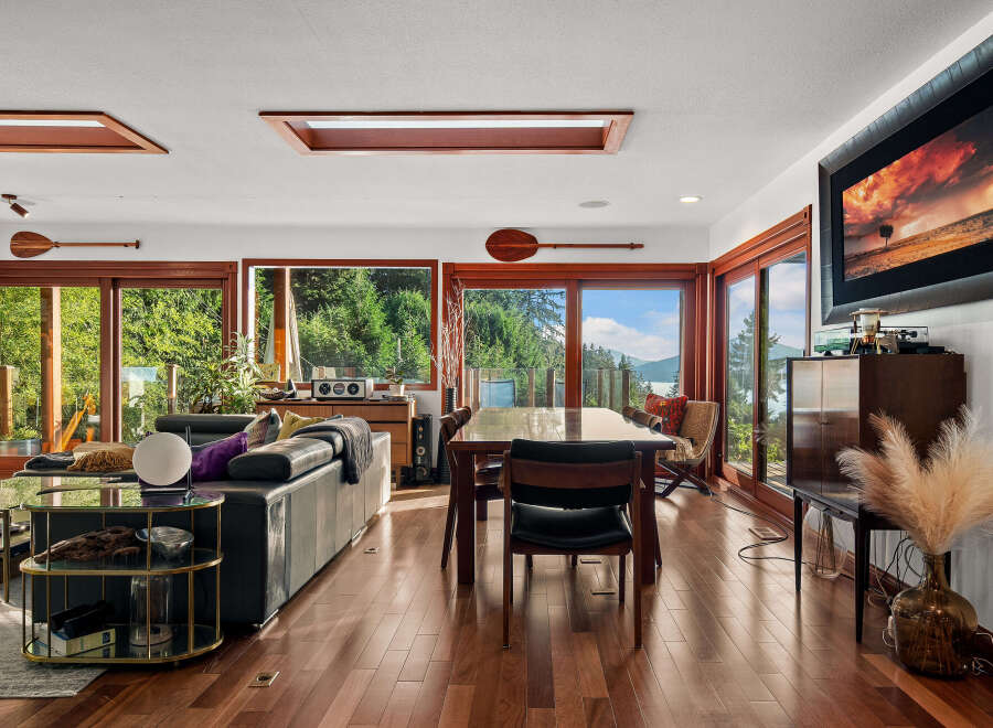Experience breathtaking natural beauty from this stunning living and dining area, featuring expansive windows that frame panoramic views of lush greenery and serene waters.