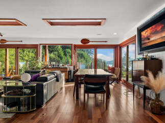 Experience breathtaking natural beauty from this stunning living and dining area, featuring expansive windows that frame panoramic views of lush greenery and serene waters.
