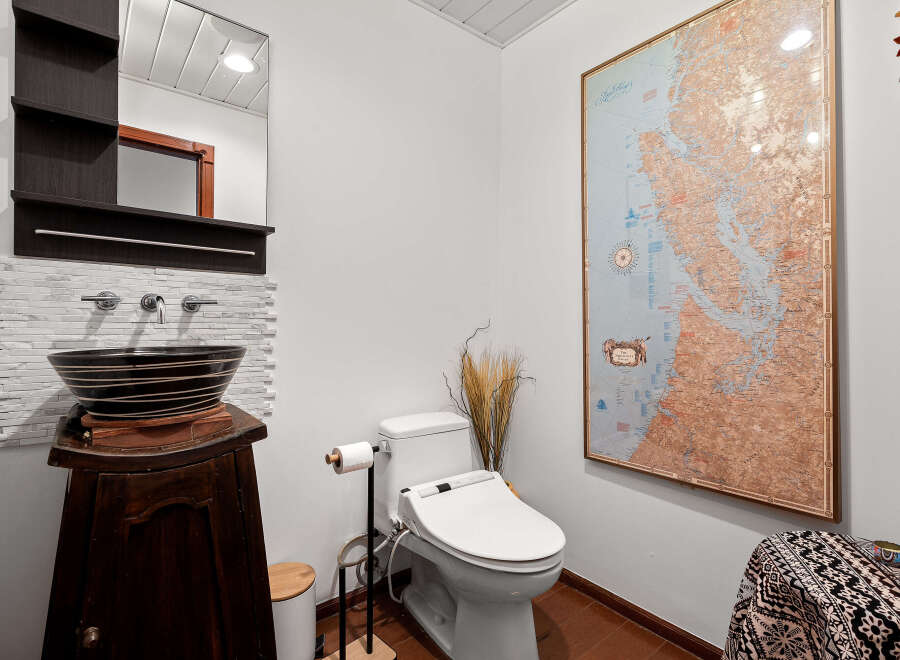 This stylish bathroom features a unique vessel sink atop a dark wood vanity, complemented by a modern bidet toilet and a striking map wall art.