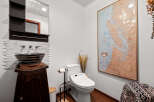This stylish bathroom features a unique vessel sink atop a dark wood vanity, complemented by a modern bidet toilet and a striking map wall art.