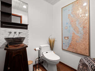 This stylish bathroom features a unique vessel sink atop a dark wood vanity, complemented by a modern bidet toilet and a striking map wall art.