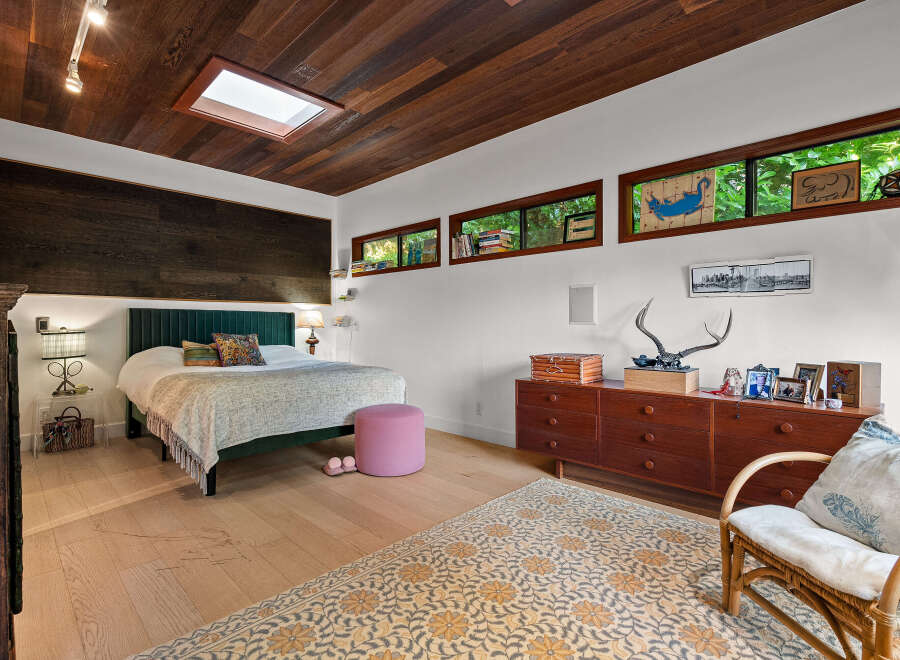 Experience a unique bedroom retreat featuring a stunning wood-paneled ceiling with a skylight, complemented by a dark wood accent wall behind the bed.