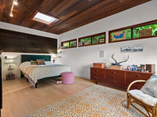 Experience a unique bedroom retreat featuring a stunning wood-paneled ceiling with a skylight, complemented by a dark wood accent wall behind the bed.
