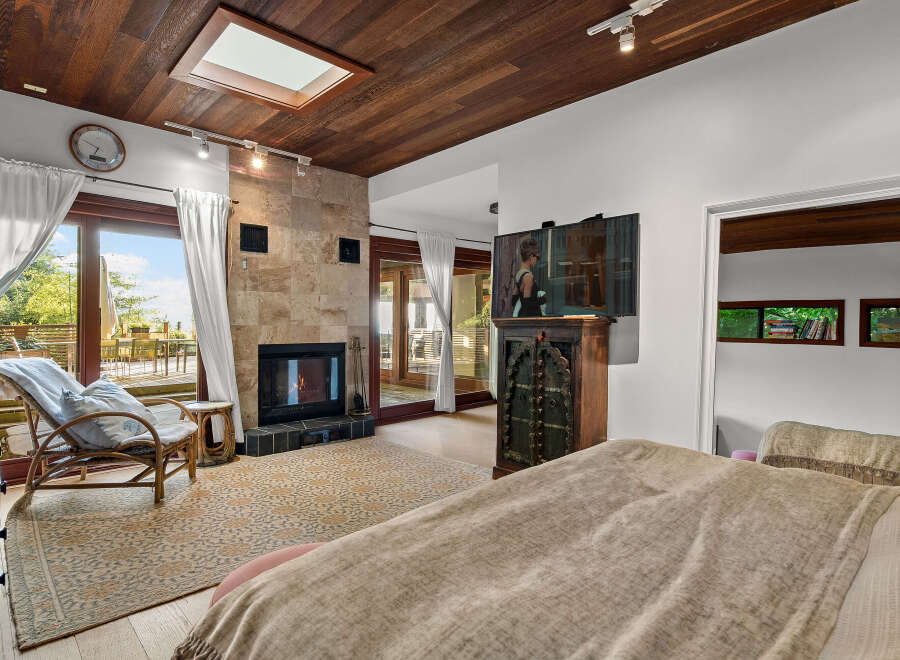 Experience luxurious living in this stunning bedroom featuring a cozy fireplace with a stone accent wall and a skylight for natural light.