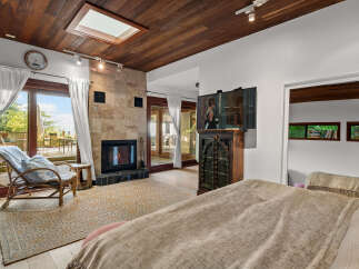 Experience luxurious living in this stunning bedroom featuring a cozy fireplace with a stone accent wall and a skylight for natural light.