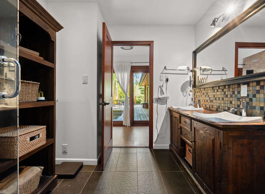 This luxurious bathroom features a rustic wooden vanity with dual vessel sinks and a mosaic tile backsplash.