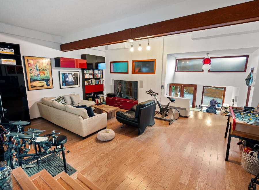 This spacious living area boasts a modern aesthetic with a large sectional sofa, a sleek black leather armchair, and an exercise bike for a healthy lifestyle.