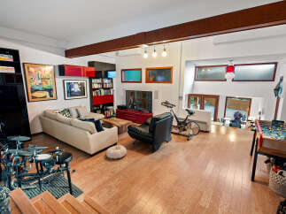 This spacious living area boasts a modern aesthetic with a large sectional sofa, a sleek black leather armchair, and an exercise bike for a healthy lifestyle.