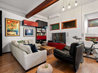 Experience modern living in this stylish living room, featuring a comfortable sectional sofa, a sleek black leather armchair, and a dedicated home gym area with a spin bike.